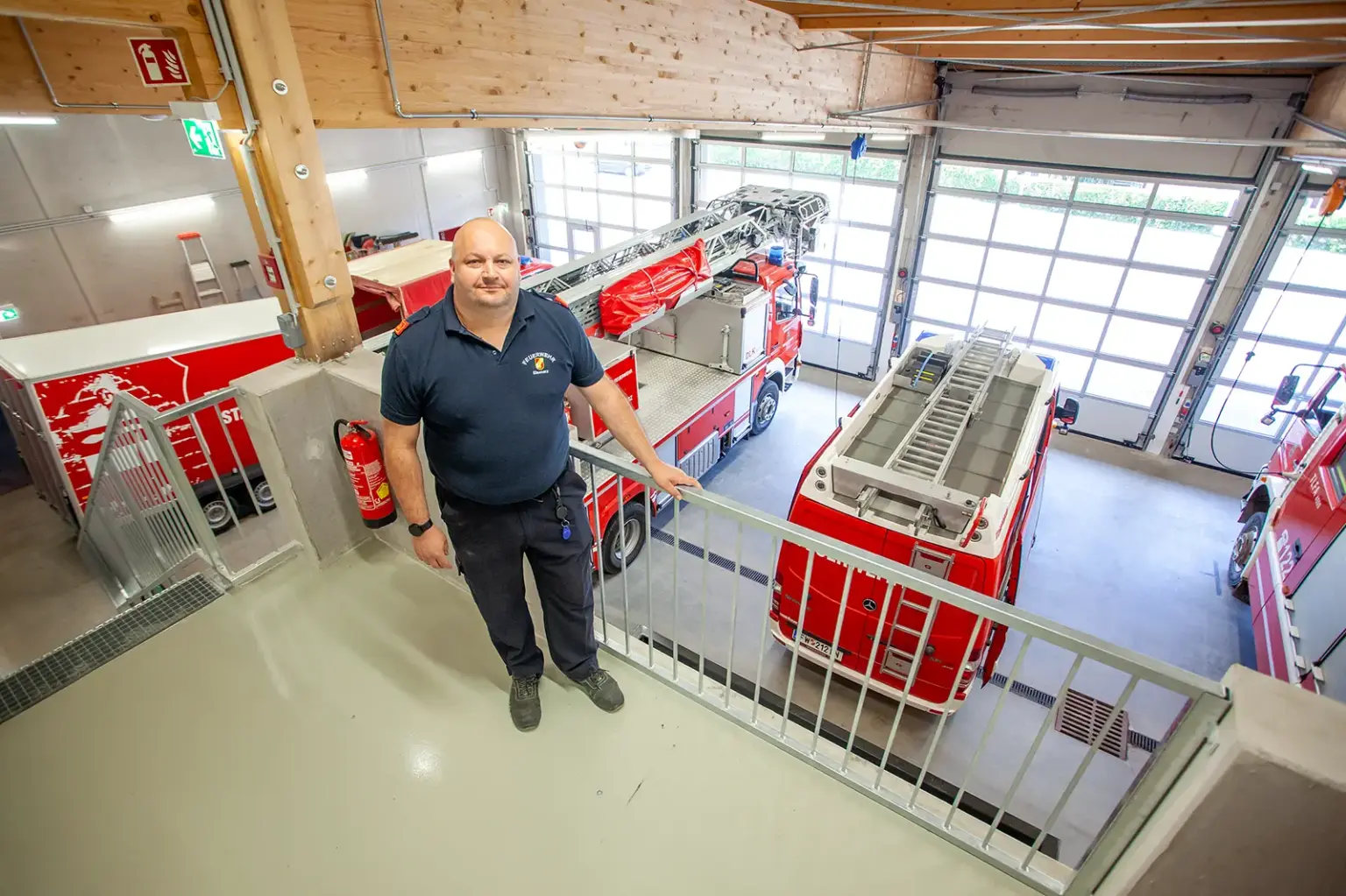Neues Eisenerzer Rüsthaus wird eröffnet Ein Mann in Feuerwehrkleidung steht an einer Brüstung in einer Halle mit großen Ausfahrtstoren und Feuerwehrfahrzeugen