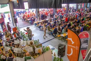 Zahlreiche Menschen sitzen in und vor einer Halle an Biertischgarnituren und hören einer Musikkapelle zu