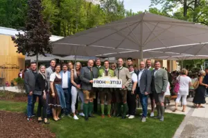 Eine große Gruppe von Personen steht mit einem Schild unter einem großen Sonnenschirm