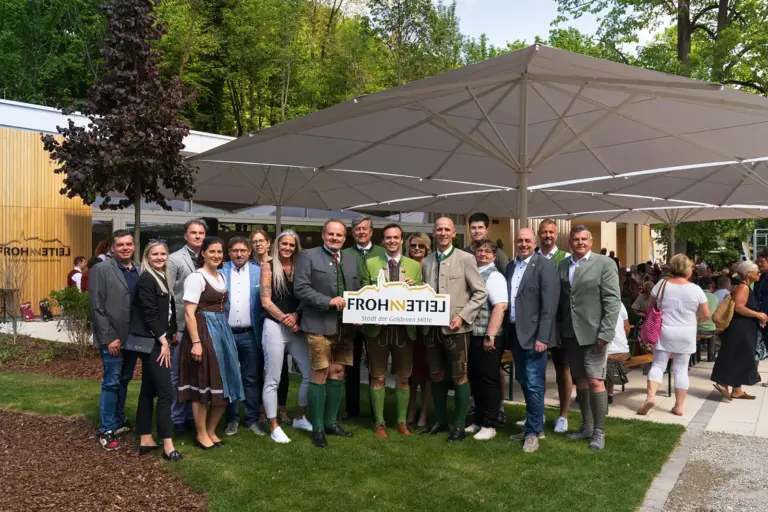 Eine große Gruppe von Personen steht mit einem Schild unter einem großen Sonnenschirm