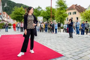 Eine Frau steht auf einem roten Teppich auf einem innerstädtischen Platz, im Hintergrund Publikum