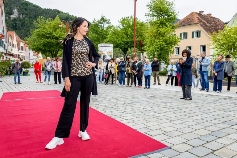 Markt, Mode & Sport in Frohnleiten: Im Mai geht’s noch richtig rund Eine Frau steht auf einem roten Teppich auf einem innerstädtischen Platz, im Hintergrund Publikum