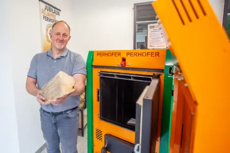 Ein Mann mit einem Holzscheit in Händen steht neben einem geöffneten Heizkessel