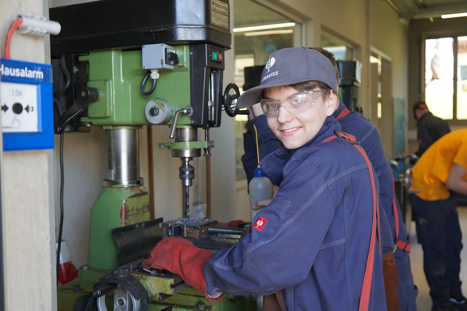 Jugendlicher in Arbeitskleidung an einer Standbohrmaschine.