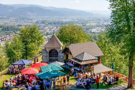 Kapfenberg: Miniwallfahrt zum Lorettofest Viele Menschen auf Bänken vor einer Bergkapelle mit schöner Aussicht.