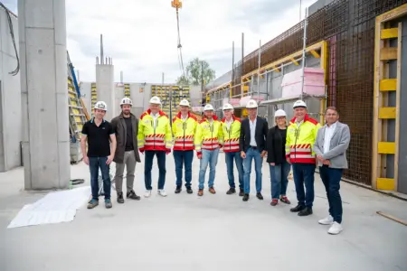 Eine Frau und mehrere Männer mit Warnwesten und Helmen auf einer Baustelle.