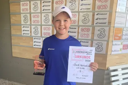 Starkes Turnier von Katharina Zmek Ein Mädchen in Sportkleidung hält bei einem Tennisturnier eine Urkunde und einen Pokal in die Kamera. Im Hintergrund sind Sponsorentafeln und Logos des Jugendcircuits zu sehen.