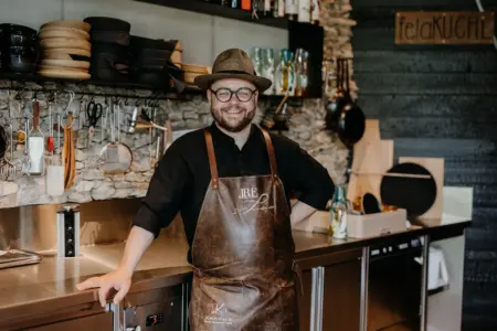 Ein Mann mit einer Kochschürze aus Leder steht vor einer Theke.