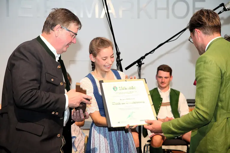 Langenwang: Harmonika-Award für Klara Mißebner Ein junge Musikerin erhält eine Urkunde von zwei Männern.