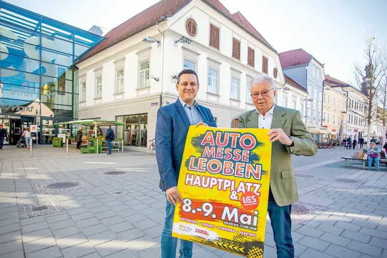 Zwei Männer stehen mit einem Plakat in Händen auf einem innerstädtischen Platz