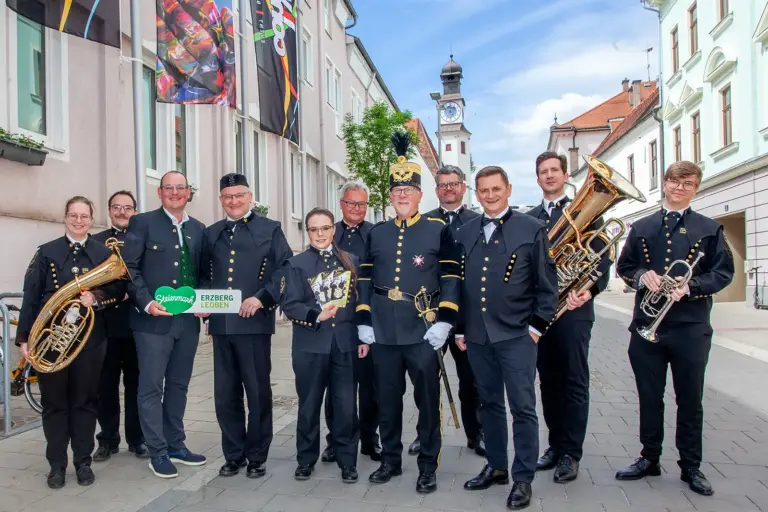 Zwölf Menschen, elf davon in Bergmannstracht, fünf mit Musikinstrumenten, stehen in einer Fußgängerzone