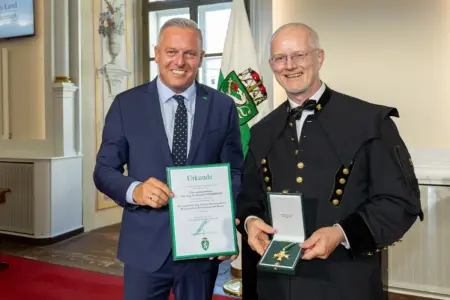Ehrenzeichen für Roland Pomberger Ein Mann im Anzug und ein Mann im Bergkittel zeigen eine Urkunde und eine Auszeichnung