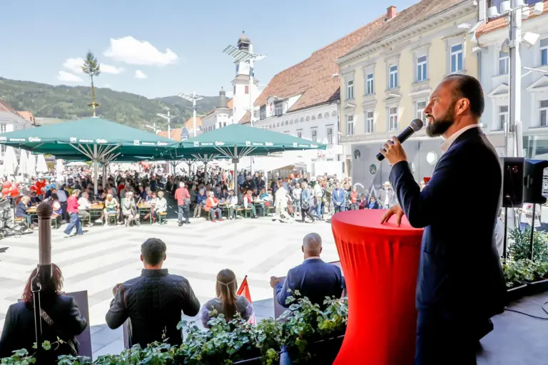 Ein Mann mit Mikrofon steht auf einem großen Platz mit vielen Menschen