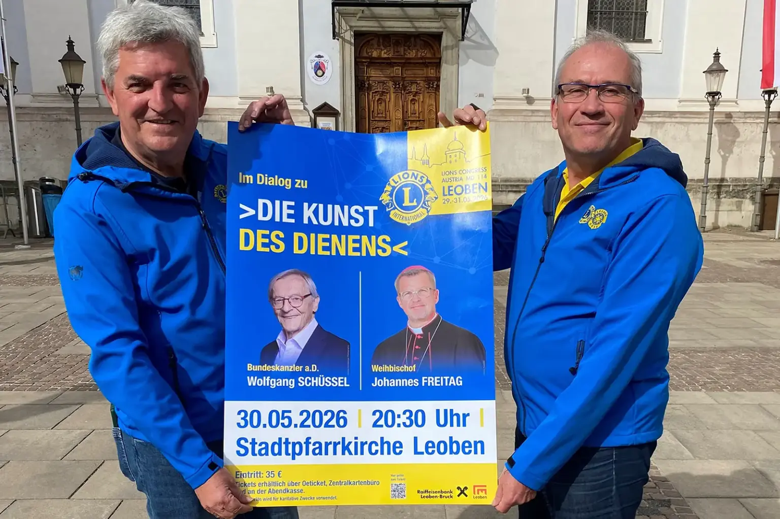 Über die Kunst des Dienens Zwei Männer in blauen Jacken halten ein Plakat