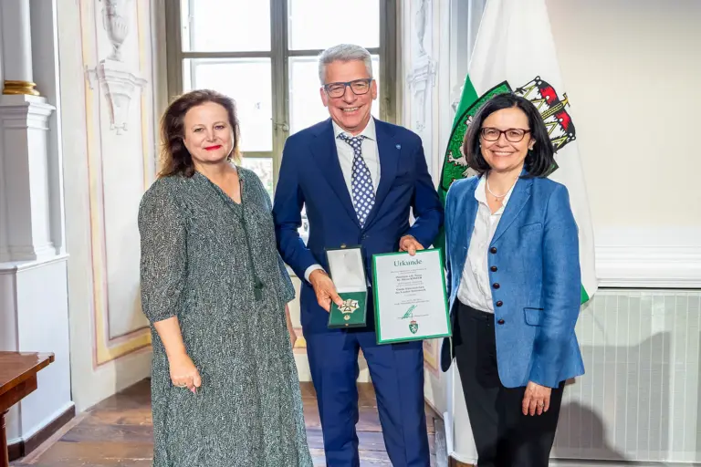 Auszeichnung für Dieter Kinzer Zwei Frauen und ein Mann präsentieren eine Medaille und eine Urkunde