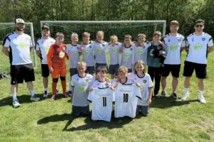 Gruppenfoto am Fußballplatz: Nachwuchsspieler und Trainer posieren vor dem Tor mit neuen Trikots nach einem erfolgreichen Turniertag.