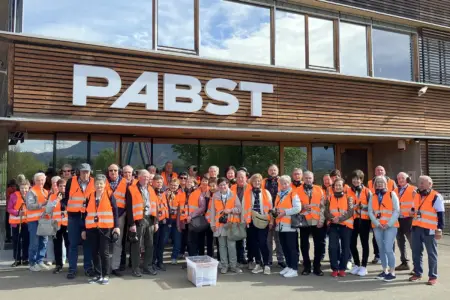 Ältere Frauen und Männer vor einem Gebäude mit Holzfassade und dem Logo der Firma Pabst.