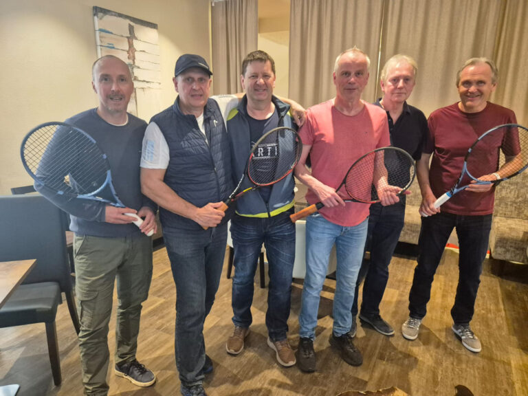 Zwei Meistertitel für den TC Kapellen Sechs Männer stehen mit Tennisschlägern in einem Innenraum nebeneinander und posieren für ein Gruppenfoto. Die Gruppe lächelt in die Kamera, während einige der Männer ihre Schläger vor sich halten.