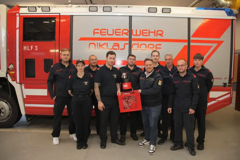 Gerätespende an die Feuerwehr Niklasdorf Mehrere Personen in Uniform stehen mit einem Gerät vor einem Feuerwehrauto