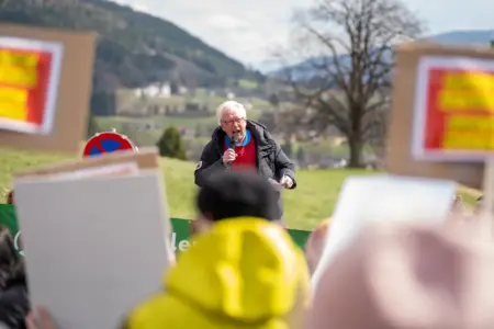 Ein Mann steht unter freiem Himmel vor Menschen mit Spruchtafeln und spricht in ein Mikrofon
