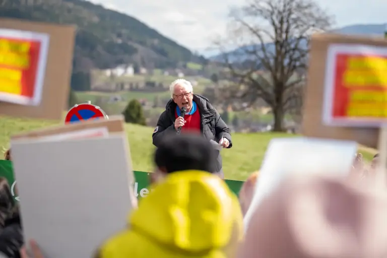 Zur Reha Aflenz: „12.700 fordern Antworten“ Ein Mann steht unter freiem Himmel vor Menschen mit Spruchtafeln und spricht in ein Mikrofon