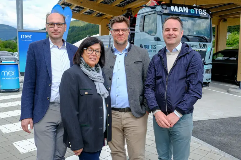 E-Tankstelle in Spital am Semmering eröffnet Vier Personen stehen bei der Eröffnung einer Tank- und Ladestation vor einem elektrischen Lkw und blicken in die Kamera. Im Hintergrund sind die überdachte Anlage sowie Berge und Bäume zu sehen.