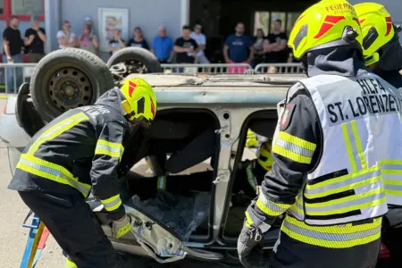 Mehrere Feuerwehrmänner stehen vor einem auf dem Dach liegenden Auto