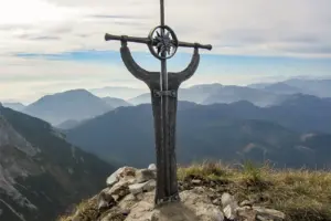 Ein kunstvoll gestaltetes Metallkreuz auf einem Berggipfel.