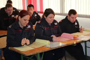 Mehrere Personen in Uniformen sitzen an Tischen und schreiben