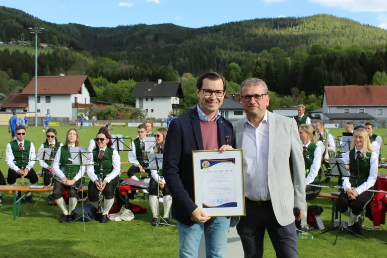 Kabinen am Sportplatz in Turnau eröffnet Zwei Männer mit Urkunde. Dahinter Musikanten.