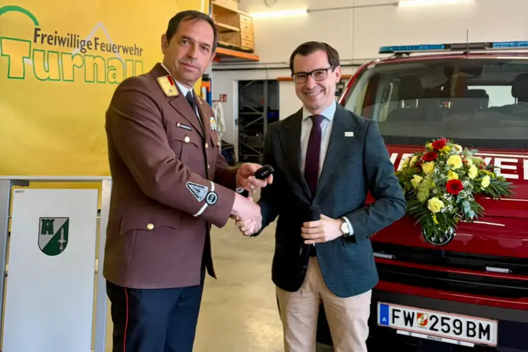 Fahrzeug für die Turnauer Feuerwehr Ein Feuerwehrmann und ein Mann in Anzug geben sich vor einem Feuerwehrauto die Hand