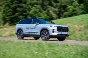Ein silbergraues Fahrzeug der Kategorie SUV fährt auf einer Landstraße von links nach rechts