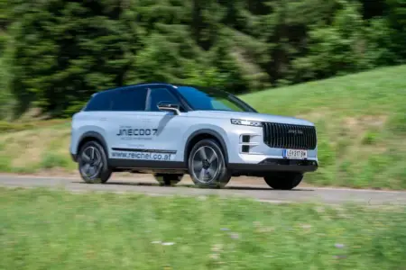 Ein silbergraues Fahrzeug der Kategorie SUV fährt auf einer Landstraße von links nach rechts