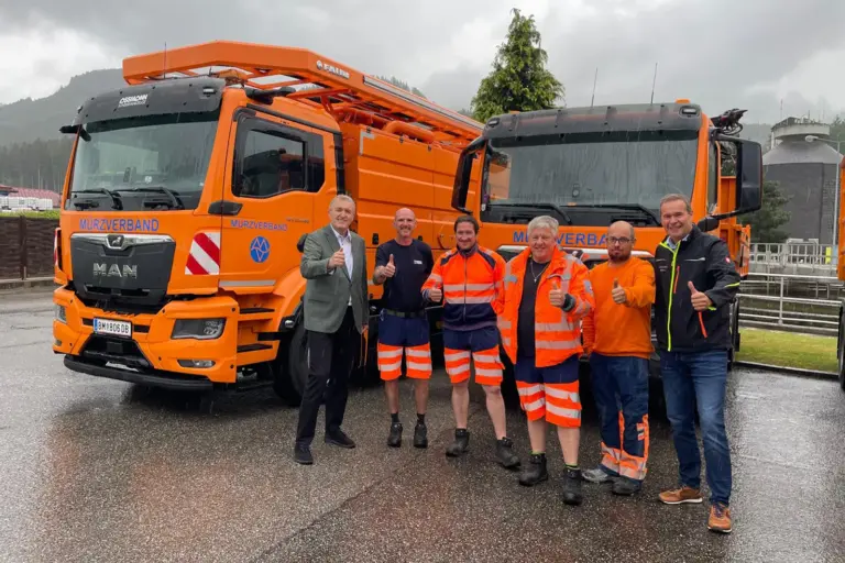 Mürzverband erweitert Fuhrpark Sechs Männer stehen vor zwei organgen Lkw