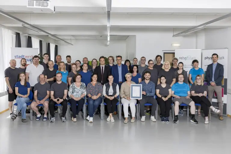 Hohe Auszeichnung für Physio und Reha Bruck Eine große Gruppe von Personen präsentiert eine Ukrunde