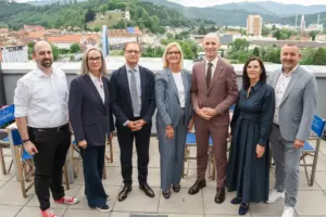 Drei Frauen und vier Männer stehen auf einer Terrasse, im Hintergrund eine Stadt