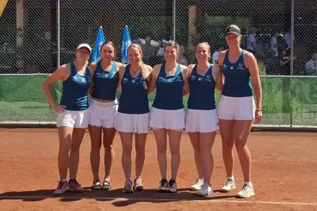 Damenmannschaft posiert vor einem Meisterschaftsspiel auf einem Tennis-Sandplatz für ein Gruppenfoto.
