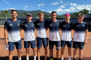 Sechs Tennisspieler stehen auf einem Sandplatz vor dem Netz und posieren für ein Mannschaftsfoto. Im Hintergrund sind Berge, blauer Himmel und die Tennisanlage zu sehen.
