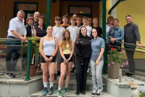 EIne Gruppe Jugendlicher steht mit einigen Erwachsenen auf einer Treppe vor einem Haus