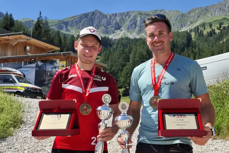 Veitsch: Traditionslauf mit zahlreichen Erneuerungen Zwei Männer mit Medaillen stehen vor einer Bergkulisse. Beide halten Pokale und geöffnete Auszeichnungsboxen mit Urkunden in den Händen und blicken in die Kamera.