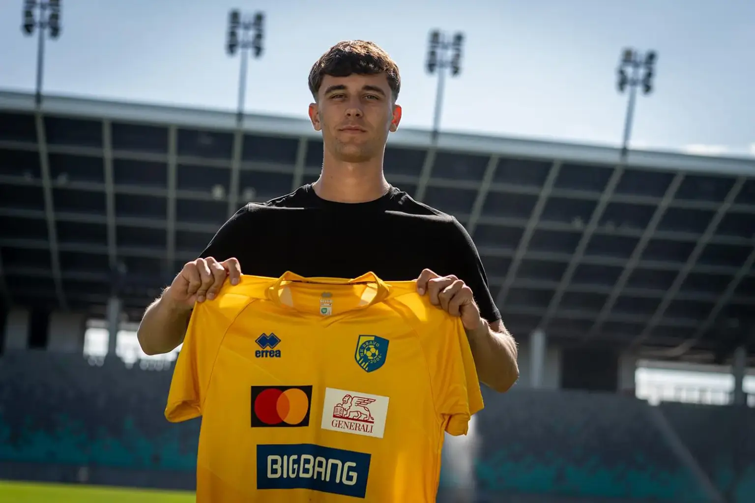 Fußballspieler präsentiert in einem Stadion sein neues gelbes Trikot nach einem Vereinswechsel.