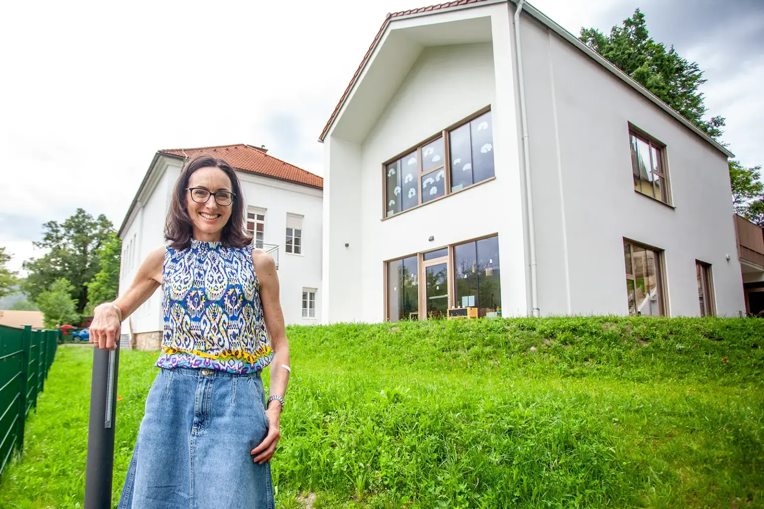 Eine Frau steht auf einer Wiese vor zwei Häusern mit weißer Fassade.