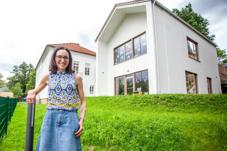 Kammern: Das große Haus der Kleinen Eine Frau steht auf einer Wiese vor zwei Häusern mit weißer Fassade.