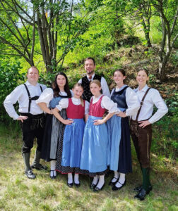Eine Gruppe von Jugendlichen und Erwachsenen in Tracht stehen unter einem Baum