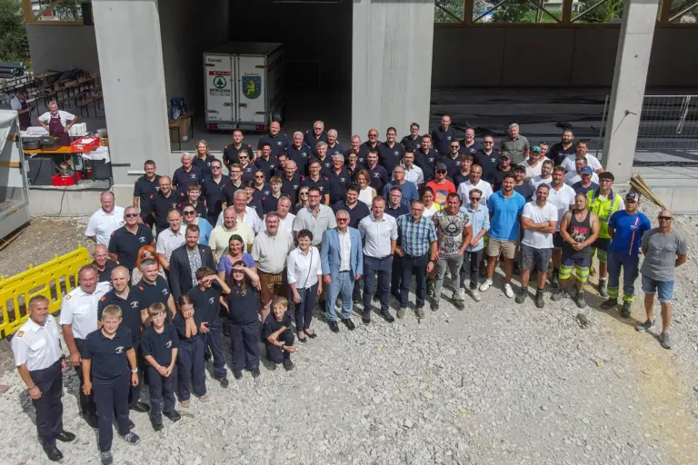 Eine große Gruppe von Personen, zum Teil in Uniform, steht vor einem Rohbau