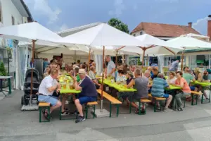 Eine Gruppe von Personen sitzt unter Sonnenschirmen an Biertischgarnituren