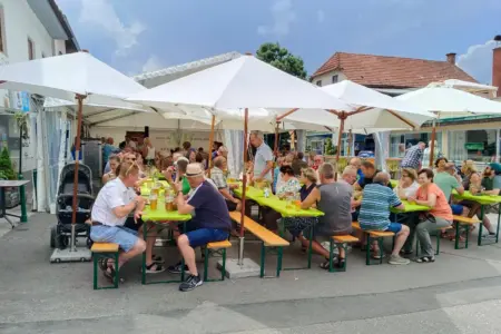 Gelungenes „Grätzlfest“-Debüt in Krieglach Eine Gruppe von Personen sitzt unter Sonnenschirmen an Biertischgarnituren