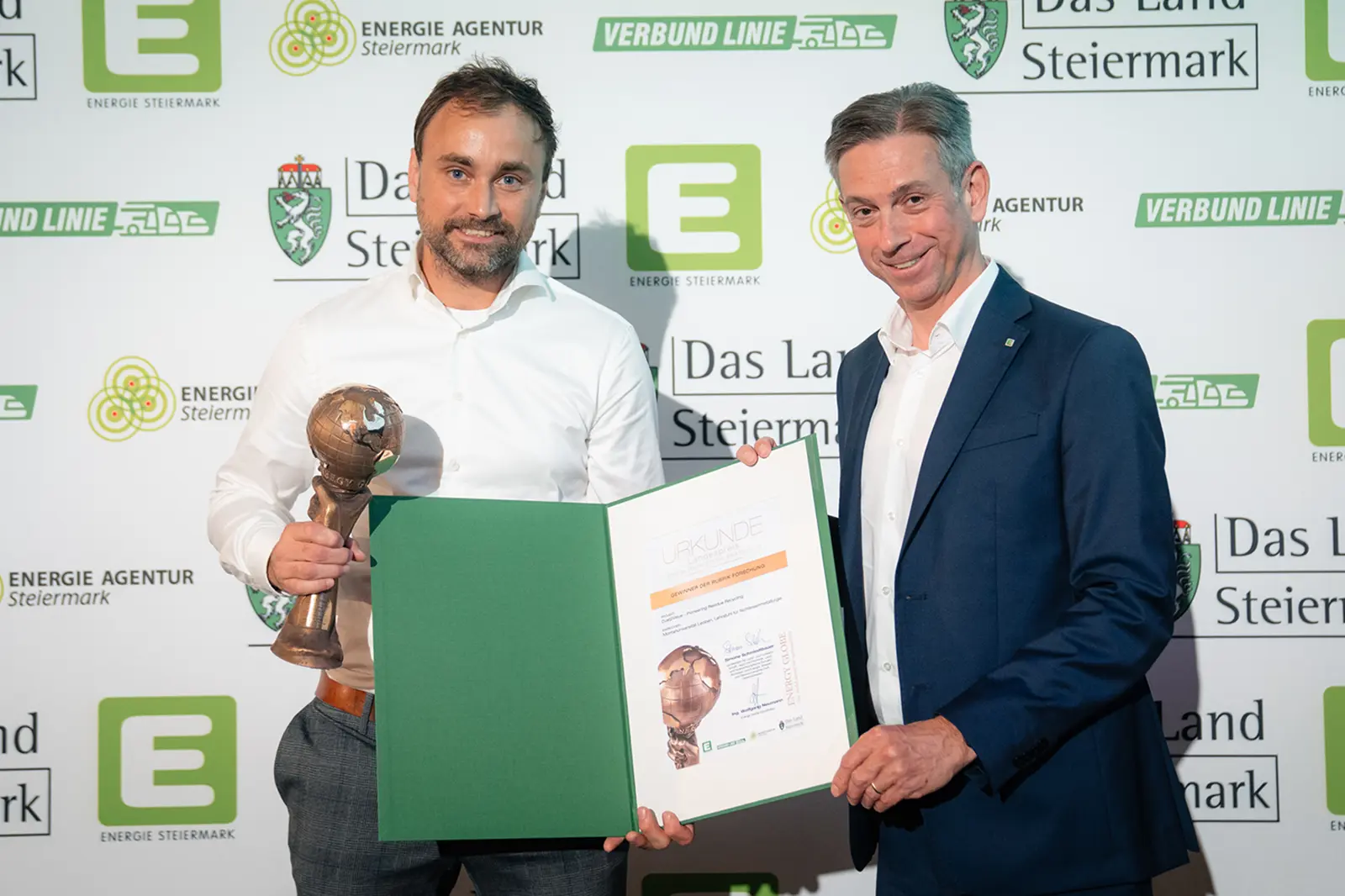 Zwei Männer präsentieren eine Trophäe und eine Urkunde