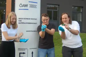 Drei Schüler mit blauen Handschuhen präsentieren Forschungsergebnis.
