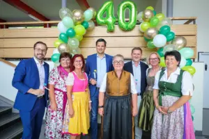 Eine Gruppe von Personen steht vor einer Wand mit Luftballons und einer aufblasbaren 40